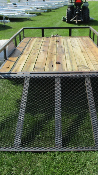 Utility Trailer with Wooden Bed on Grass Featuring Metal Ramp